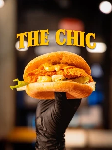 Visuel The Chic : burger au poulet croustillant tenu dans une main gantée