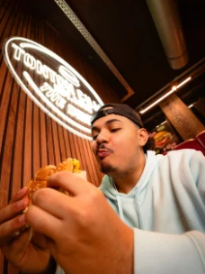 Client dégustant un burger sous l'enseigne lumineuse Tonton Chami