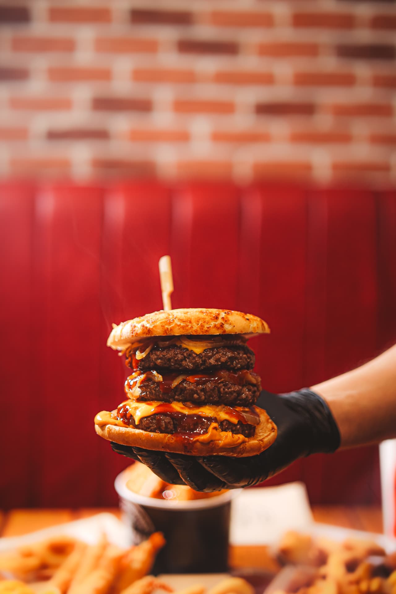 Burger triple steak Tonton Chami tenu en main devant une banquette rouge
